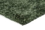 Een close-up van de hoek van het New Paulo Dark Green 442 170x230 vloerkleed toont de dikke shaggy vezels met textuur tegen een witte achtergrond.