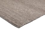 Close-up van het geweven beige oppervlak van het vloerkleed Valentino Taupe 820 200x300 met dikke stiksels langs de rand, getoond op een witte achtergrond.