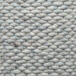 Close-up van het Genua Mint Green 428 200x300 vloerkleed. Het geweven weefsel met dikke garens in een zich herhalend ovaal patroon is getextureerd. Het materiaal ziet er zacht en donzig uit, vergelijkbaar met een handgeweven wollen textiel.