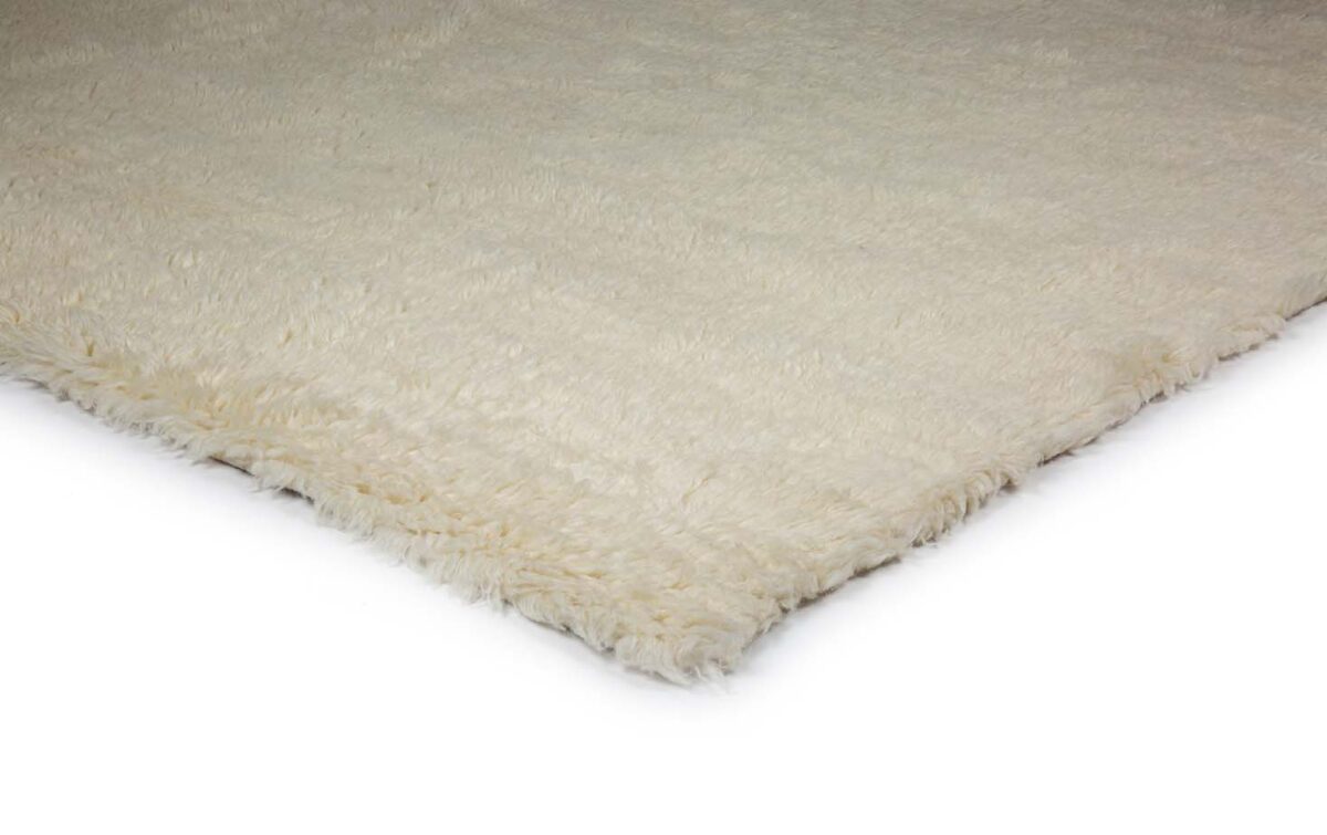 Een close-up van de hoek van het Merano White 011 200x300 pluizige, gebroken witte shagtapijt op een witte achtergrond.