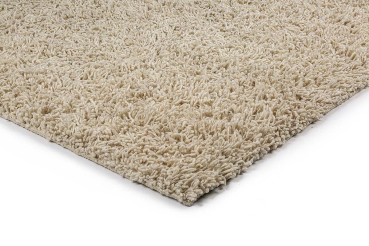 Close-up van de hoek van het Berbero Lungo Cloud White 815 vloerkleed (170x230), met de dikke beige shaggy vezels tegen een witte achtergrond.