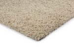 Close-up van de hoek van het Berbero Lungo Cloud White 815 vloerkleed (170x230), met de dikke beige shaggy vezels tegen een witte achtergrond.