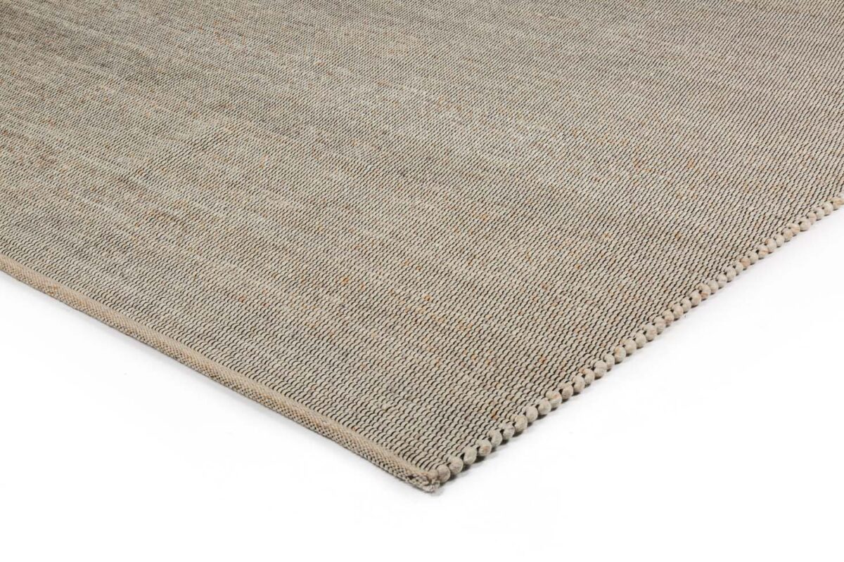 Een close-up van de hoek van het Bressano Light Beige 141 200x300 vloerkleed benadrukt het geweven oppervlak met textuur en de gedetailleerde stiksels aan de randen.