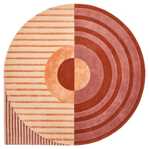 De Fano Girare Lychee ø280 is een rond tapijt dat in tweeën is gesplitst: de ene kant heeft perzik en beige strepen, de andere kant toont concentrische cirkels in rood en roze, die een gedurfd geometrisch patroon vormen met een moderne uitstraling.