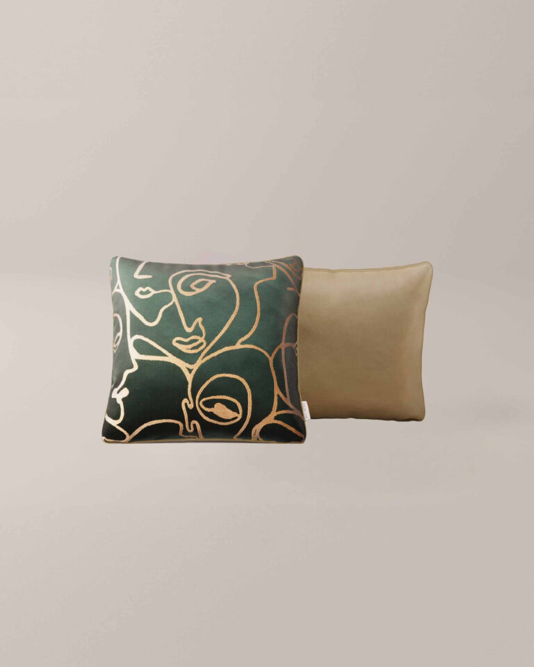 Twee vierkante sierkussens van Henri Emerald - de ene met een abstract gezicht van gouden lijnen op een donkergroene achtergrond, de andere effen beige - op een neutrale achtergrond.
