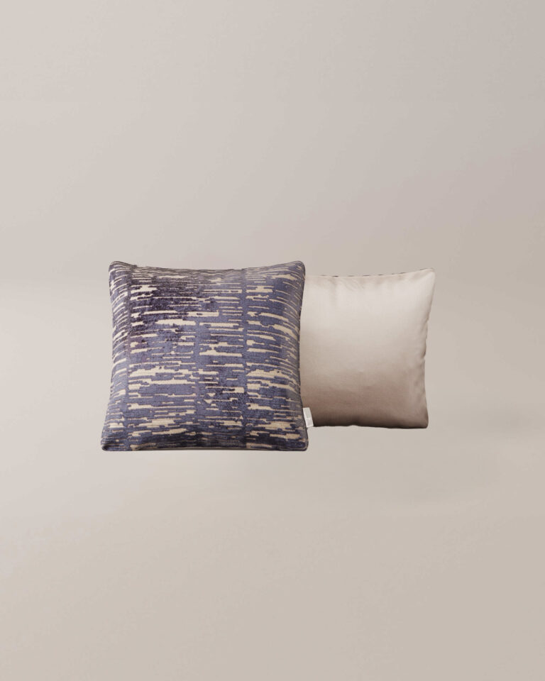 Het Indigo sierkussen heeft een abstract blauw en beige patroon met textuur naast een effen lichtbeige kussen met een glad oppervlak, beide op een neutrale achtergrond.