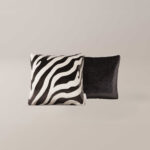 Twee vierkante kussens van Zebra: de ene heeft een zwart-witte zebraprint, de andere is effen zwart, beide naast elkaar geplaatst tegen een effen lichte achtergrond.