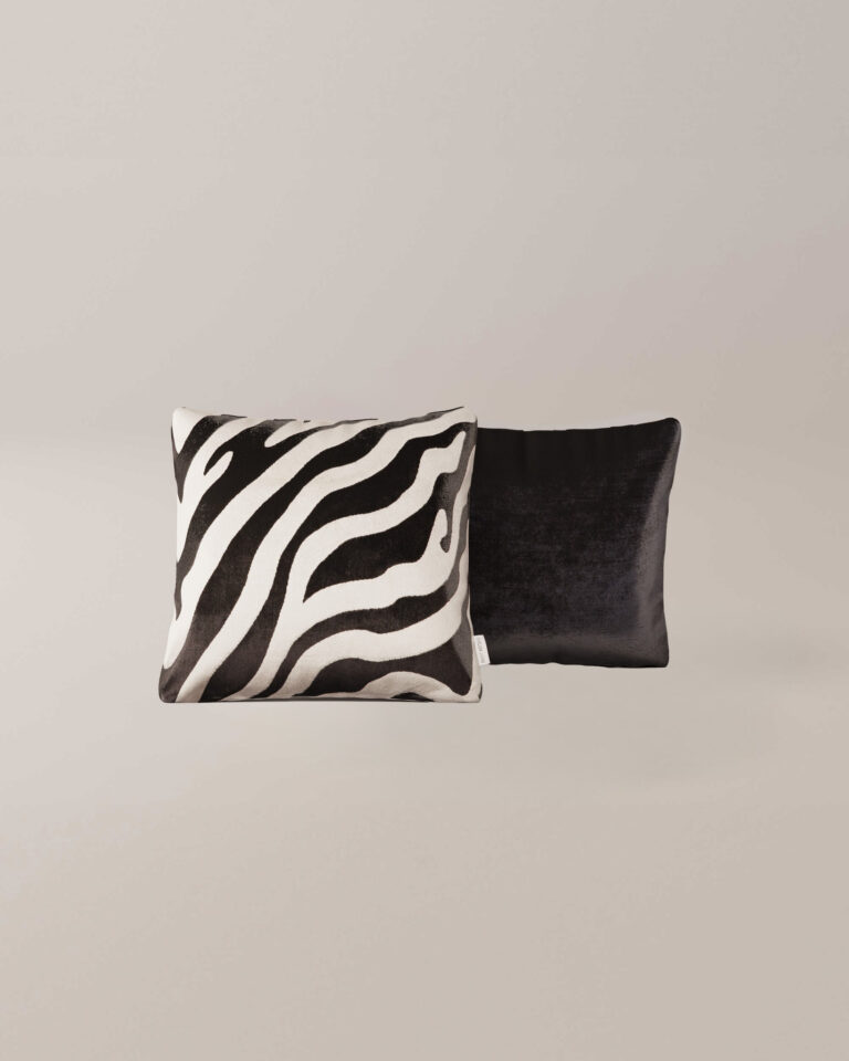 Twee vierkante kussens van Zebra: de ene heeft een zwart-witte zebraprint, de andere is effen zwart, beide naast elkaar geplaatst tegen een effen lichte achtergrond.