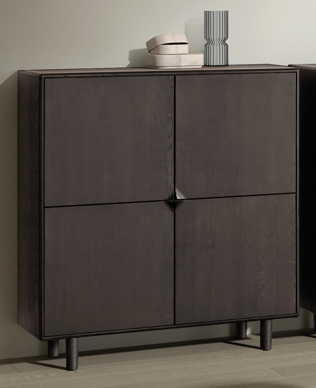 De SENTO BARKAST EL55, een moderne donkerhouten kast met vier deuren en hoge poten, staat tegen een lichte muur. Bovenop staan twee gestapelde beige dozen en een hoge decoratieve gestreepte vaas.