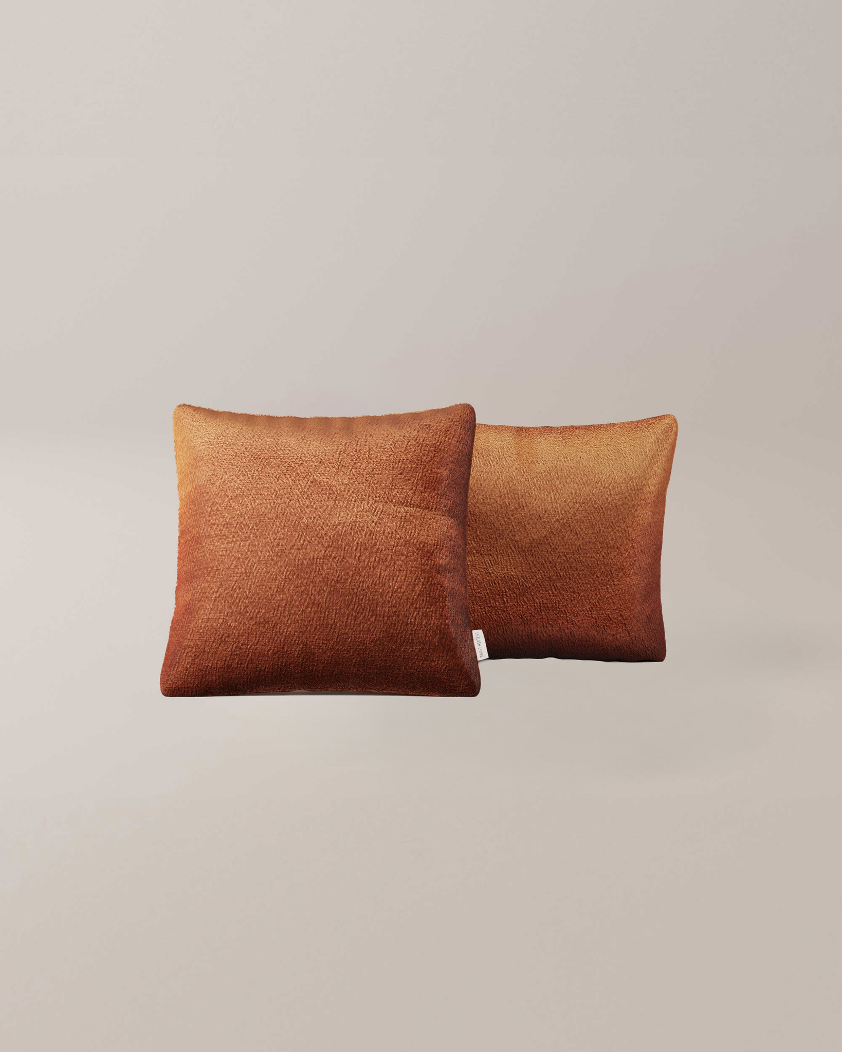 Twee vierkante Derby-kussens met een structuurverloop in warme bruine en oranje tinten tegen een effen, lichtgekleurde achtergrond.