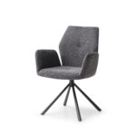 De Stoel Chris Blue Grey / Brego 16 is een moderne, blauwgrijs gestoffeerde stoel met een hoge rug, schuine armleuningen en een zwart metalen vierpoots draaivoet, tegen een witte achtergrond.