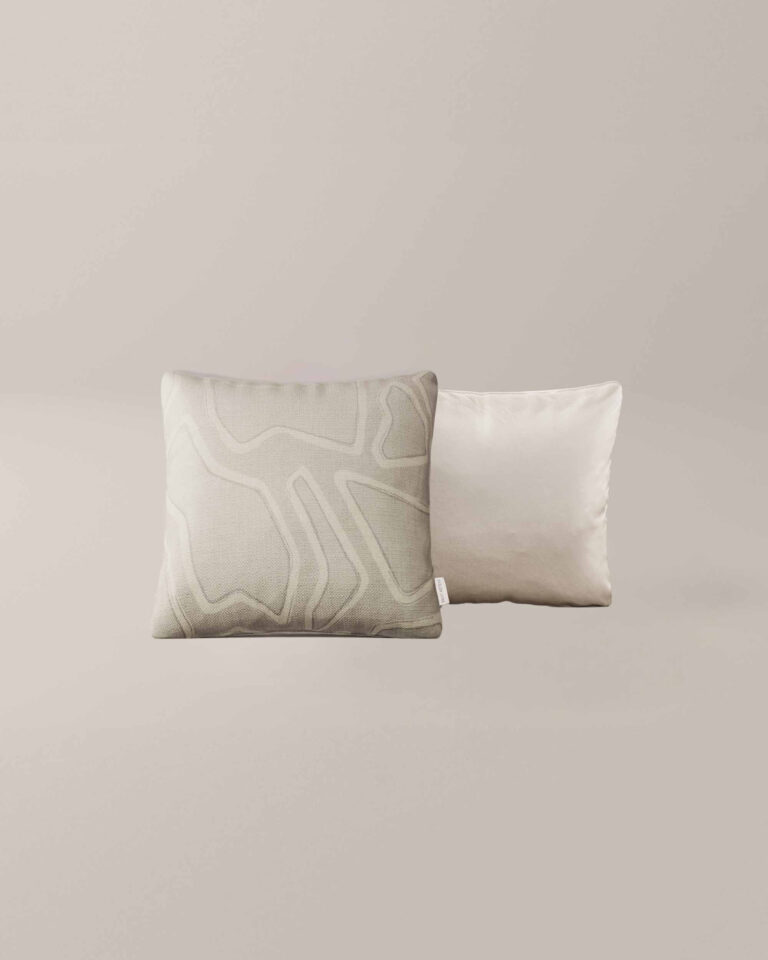Twee vierkante Rocky Roads sierkussens op een neutrale achtergrond; het voorste kussen is lichtgrijs met een abstract lijnenpatroon en het achterste kussen is effen beige of gebroken wit.