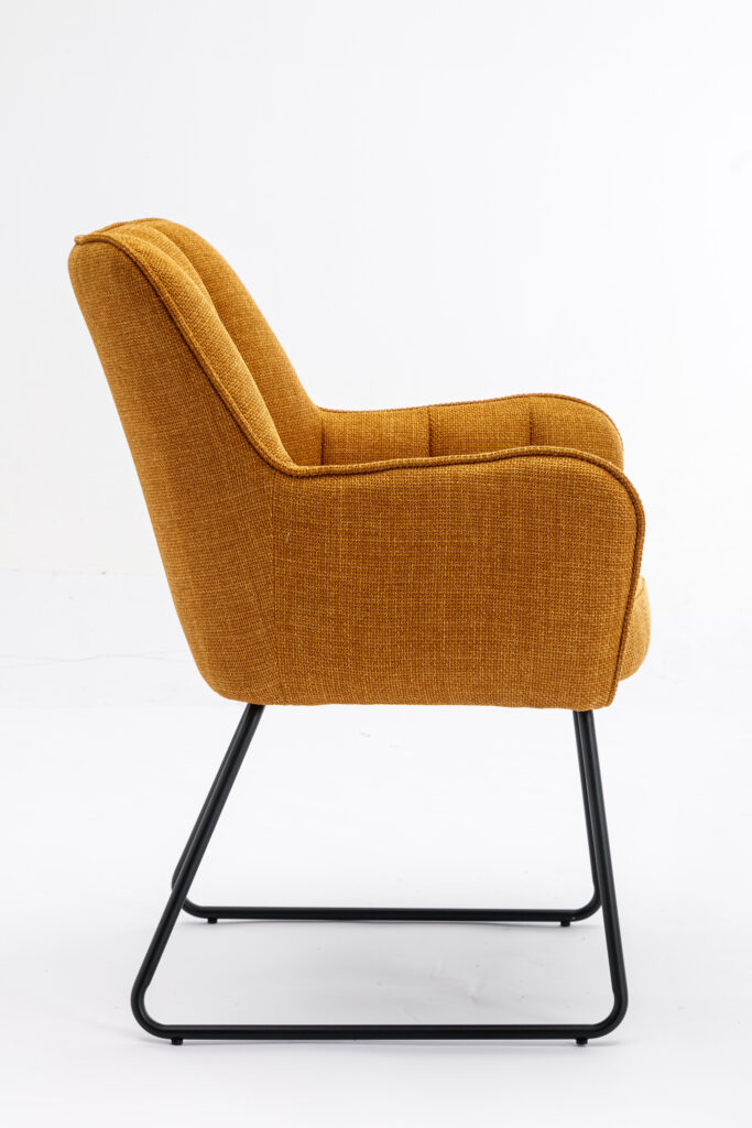 Zijaanzicht van de Eetkamerstoel Kevin Bjorn Fabric Mustard stoel met mosterdgele bekleding, zwarte metalen poten, een gebogen rugleuning en gevoerde armleuningen, tegen een effen witte achtergrond.