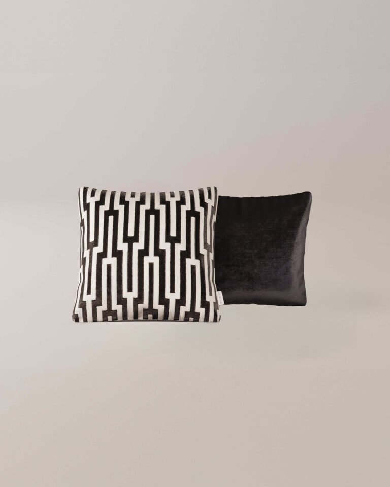 Twee Athena sierkussens: een met een gedurfd zwart-wit geometrisch patroon, de andere in effen zwart met een subtiel glanzende fluwelen textuur, worden geplaatst tegen een effen lichte achtergrond.