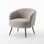 De Laura fauteuil Stof Teddy Natural 01 heeft een bekleding van natuurlijke teddystof, een afgeronde rugleuning en slanke zwarte metalen poten, tegen een effen witte achtergrond.