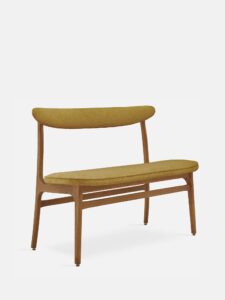 De 200-190 Bank Boucle Mustard Dark Wood heeft een mid-century modern ontwerp met een gebogen mosterdgele gestoffeerde zitting en rugleuning, slanke donkerhouten poten en een minimalistische stijl, tegen een effen witte achtergrond.