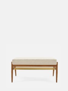 De FOX Bench 90 heeft een zitting met boucle crèmekleurige kussens, een frame van donker hout en een blad van goudkleurig metaal met latten tegen een effen witte achtergrond.