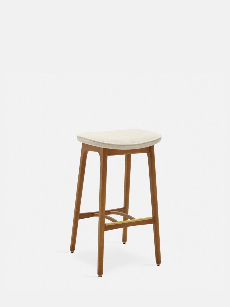 De 200-190 Barkruk Basic M/75 Boucle Creme Dark Wood heeft een minimalistisch ontwerp met vier schuine donkerhouten poten, een lichtbeige gebogen zitting en een gouden dwarsbalk voor ondersteuning, tegen een effen witte achtergrond.
