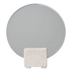 De Tafelspiegel heeft een rond, helder oppervlak dat rechtop wordt ondersteund door een rechthoekige, lichtgekleurde stenen voet tegen een sobere achtergrond.