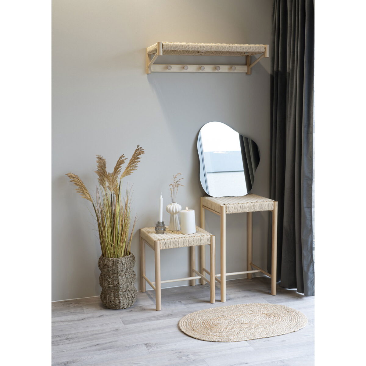 Een minimalistische kamer is voorzien van een geweven vloerkleed, twee in elkaar geschoven rieten tafels met kaarsen en een vaas, de Palermo spiegel (50x55 cm), een wandplank met haken en een grote mand met gedroogd gras in neutrale tinten. Donkere gordijnen omlijsten het tafereel.