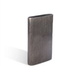 De Vaas Ovaal Loodkleurige 34 is een hoge, rechthoekige metalen vaas met een smalle ovale opening en verticale gestructureerde ribbels op een witte achtergrond.