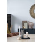 Een brandende witte kaars, een ronde zwart/witte keramieken vaas (Ø9,5x20 cm), gedroogde bloemen, twee kleine beeldjes en een decoratieve steen staan op een lichte houten tafel in een moderne, minimalistische kamer met neutrale tinten.
