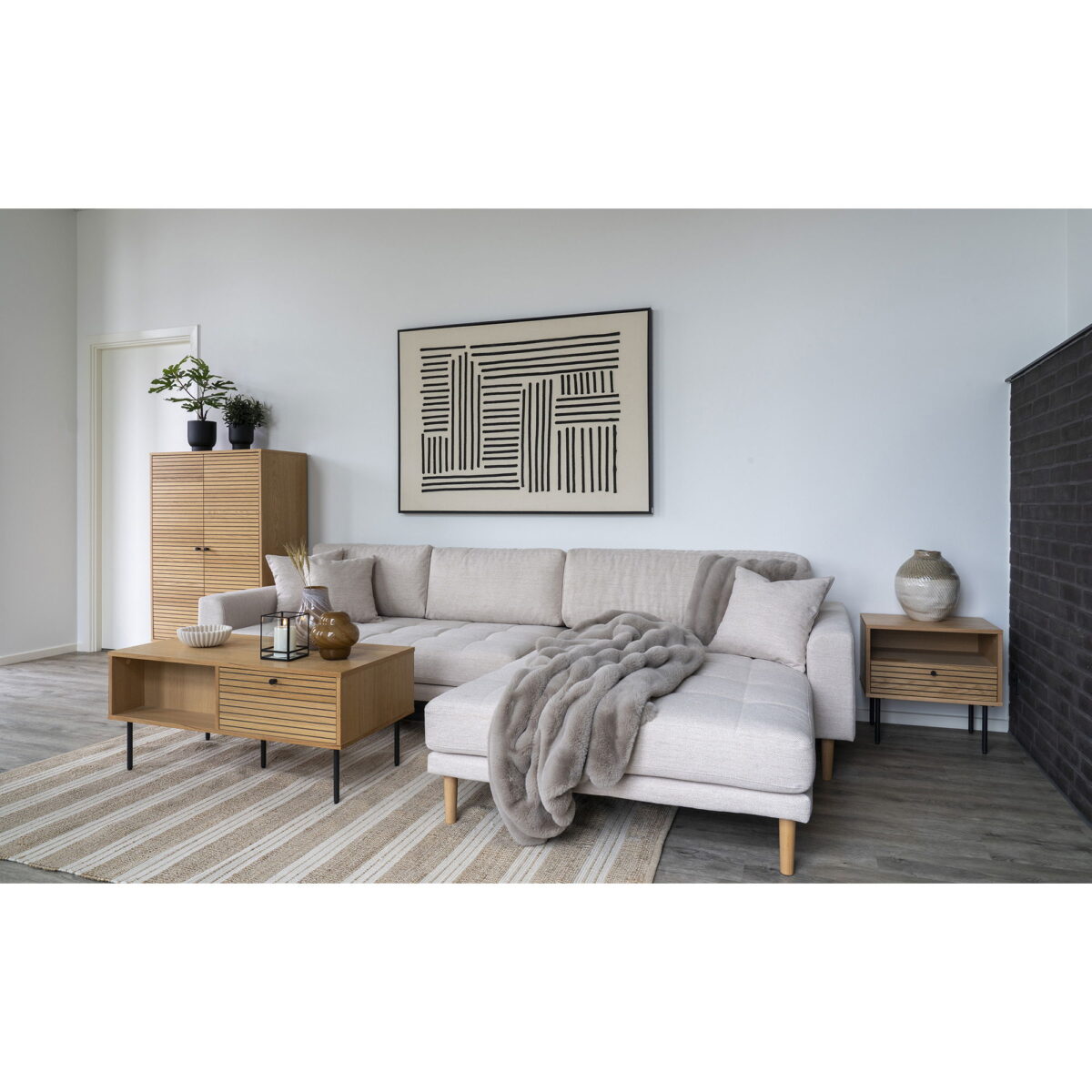 Een moderne woonkamer met een lichtbeige sofa, houten salon- en bijzettafels, een kast met planten, een gestreept vloerkleed, gezellige grijze plaids, abstracte zwart-witte muurkunst en een stijlvolle vaas.