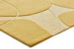 Een close-up van het Bolsena Wild Wonder 200x300 tapijt toont het geometrische patroon in geel en crème, met gestructureerde en gladde delen met gebogen lijnen en verhoogde details. De schuine foto benadrukt de dikte en het unieke ontwerp van het tapijt.