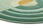 Een close-up van het Fano Girare Green ø200 tapijt, een modern rond design met groene, crèmekleurige en gele geometrische patronen, waaronder concentrische strepen en een gele halve cirkel in het midden.