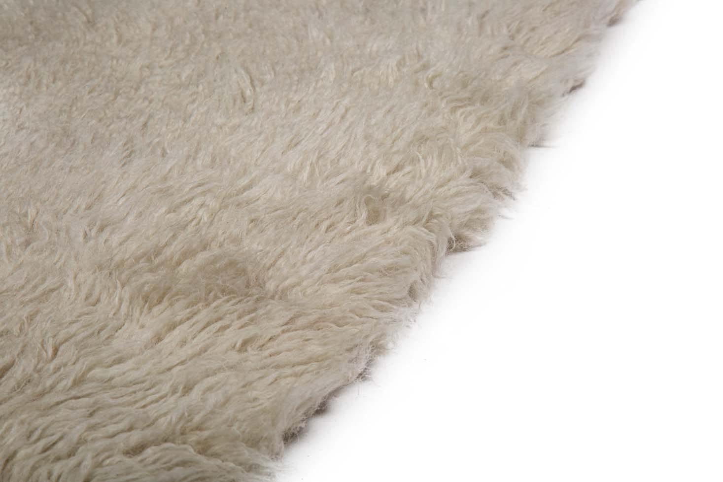Close-up van de rand van het Merano Silver 012 170x230, een zacht, beige, donzig tapijt op een witte achtergrond.