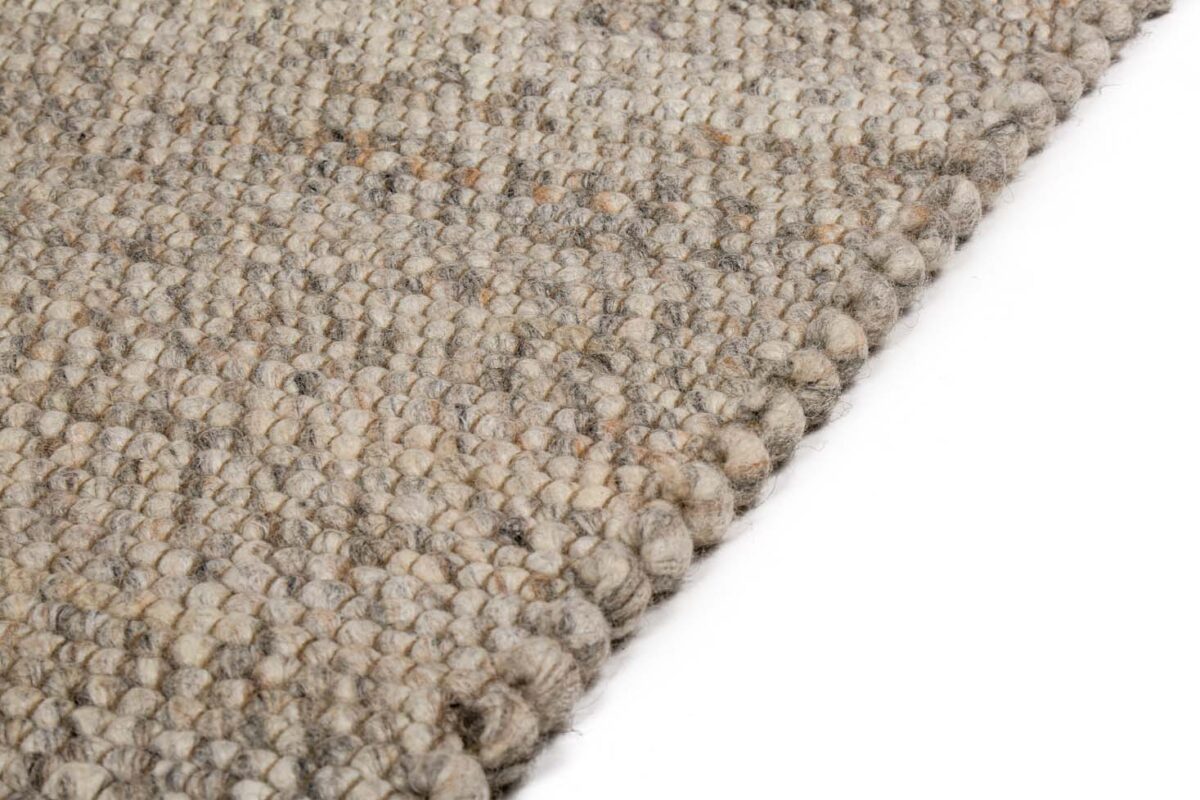 Close-up van het Verona ST Natural Grey 834 170x230 tapijt, met dikke beige en grijze vezels in een geweven textuur, schuin afgebeeld op een witte achtergrond.
