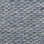 Close-up van Genua Sky Blue 227 170x230: een geweven stof met dikke, getextureerde garens die een grof, gevlochten patroon vormen. Het zachte, licht pluizige oppervlak toont subtiele kleurvariaties in de vezels.
