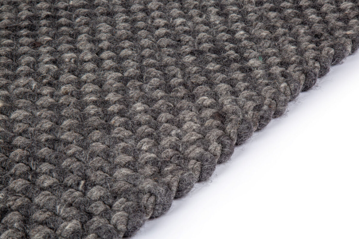 Close-up van het Burano Anthracite 614-604 vloerkleed (170x230), een donkergrijs geweven stof met textuur en dikke, afgeronde garenlussen, schuin afgebeeld op een witte achtergrond.