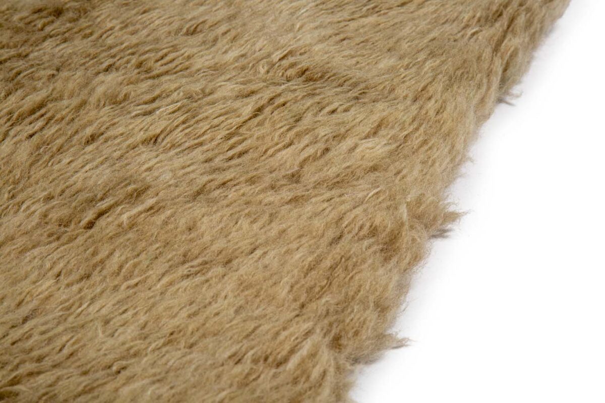 Close-up van Merano Beige 002 170x230, een bruine, gestructureerde, harige stof met een zacht, golvend oppervlak, gedeeltelijk afgebeeld tegen een witte achtergrond.