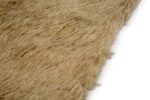 Een close-up van het Merano Beige 002 200x300 tapijt toont het lichtbruine, ruige en getextureerde oppervlak dat lijkt op imitatiebont of wol, tegen een witte achtergrond.