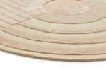 Een close-up van de Fano Girare White Beige ø200, een rond tapijt met gestructureerde concentrische lijnen en een groot centraal cirkelvormig patroon, getoond op een witte achtergrond.