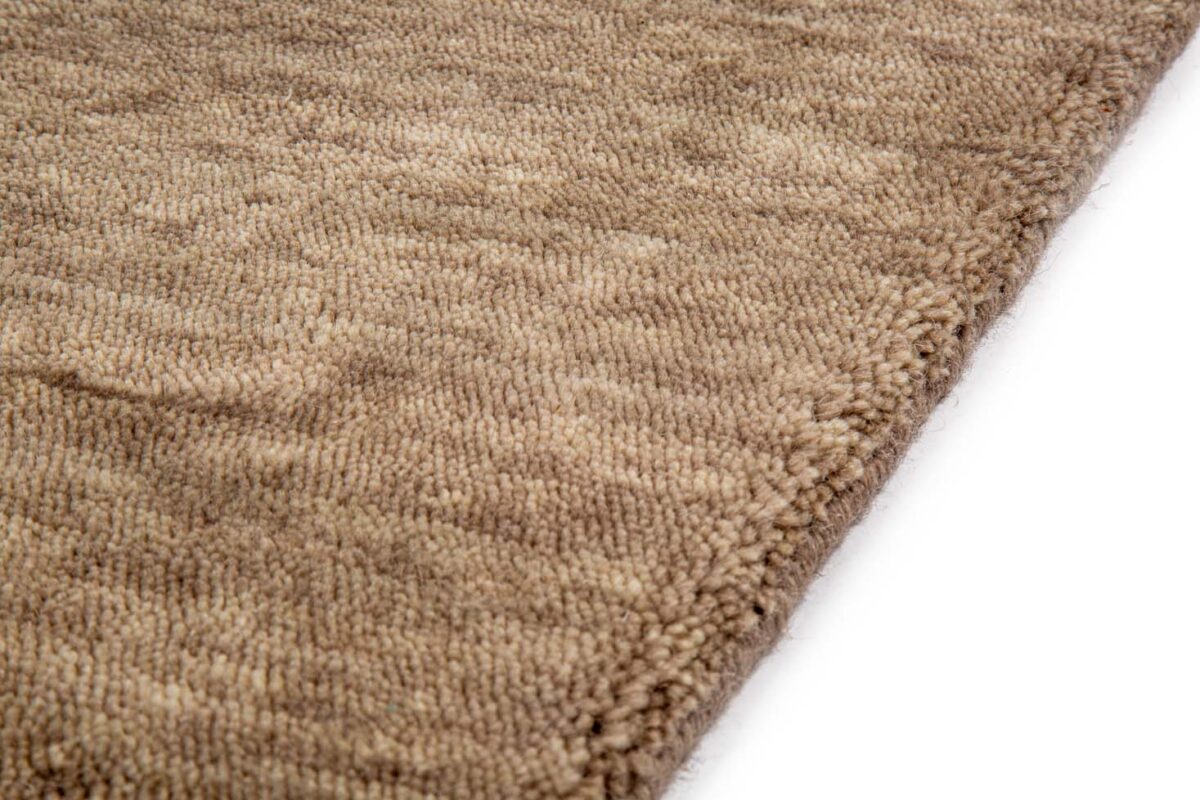 Een close-up van het San Stefano Camel 09 170x230 tapijt toont het beige, getextureerde weefsel en de dikke, zachte pool, schuin gefotografeerd op een witte achtergrond.