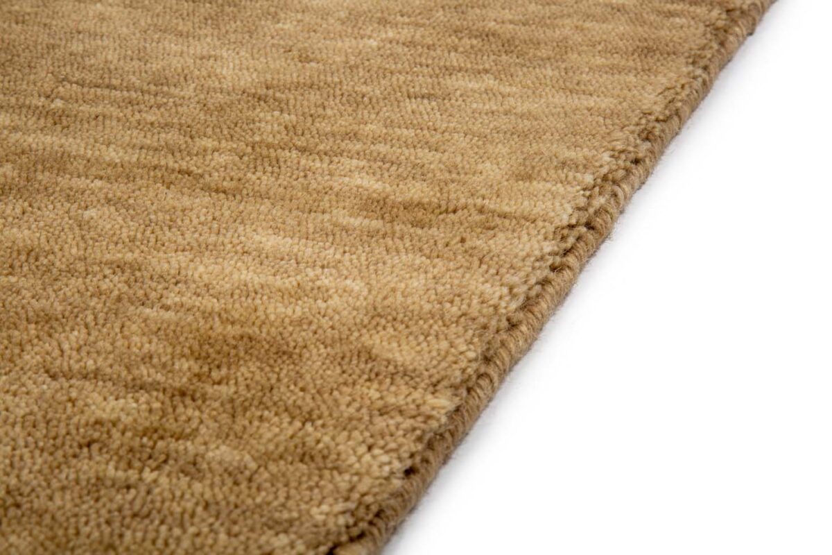 Close-up van het San Stefano Dark Beige 08 200x300 vloerkleed, met een taankleurig, gestructureerd oppervlak met een subtiel, onregelmatig patroon. Een hoek van het tapijt is te zien tegen een witte achtergrond.