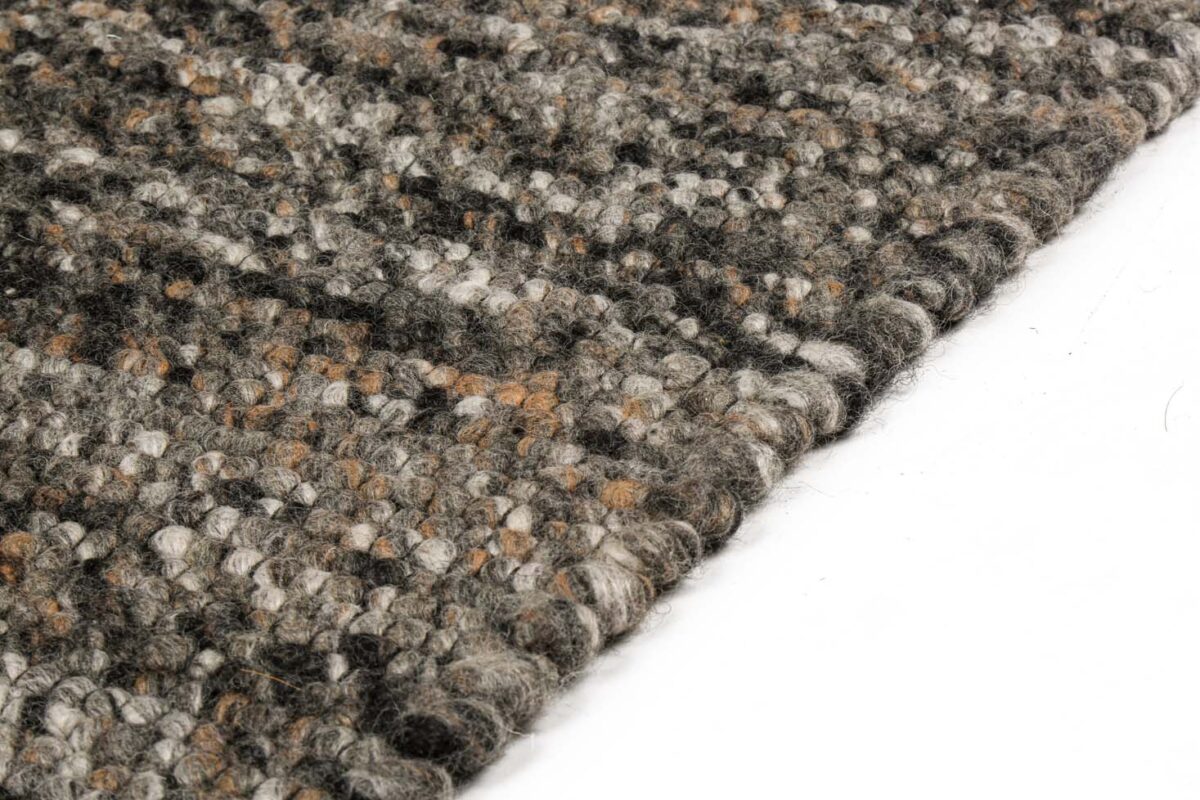 Close-up van het Verona ST Brown Grey 940 200x300 tapijt, met een structuurweefsel van grijze, zwarte, bruine en crèmekleurige garens, schuin afgebeeld op een witte achtergrond.