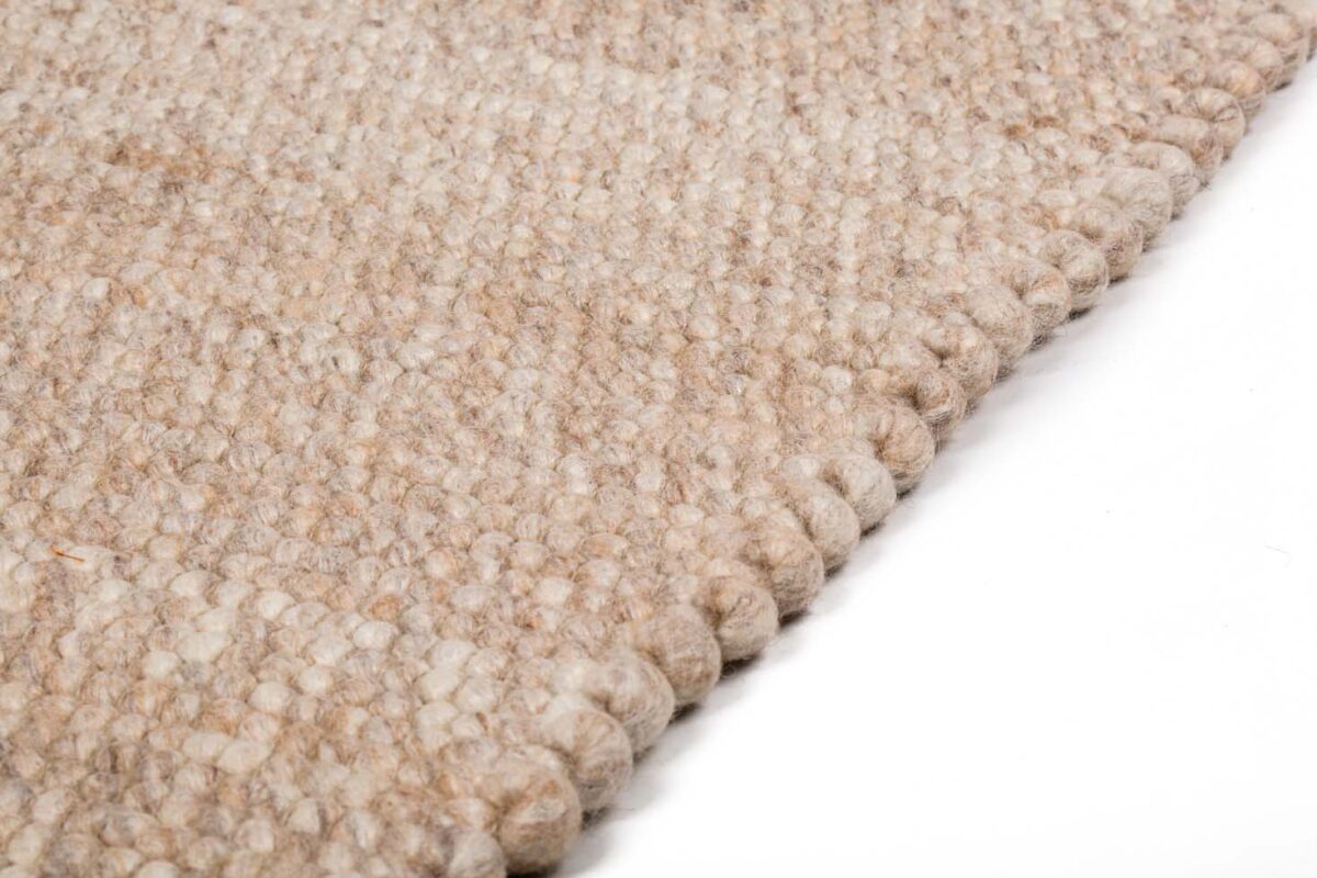 Close-up van het Verona ST Beige 142 200x300 tapijt, met een grove, geweven lusstructuur in beige, schuin afgebeeld tegen een witte achtergrond.