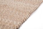 Close-up van het Verona ST Beige 142 200x300 tapijt, met een grove, geweven lusstructuur in beige, schuin afgebeeld tegen een witte achtergrond.