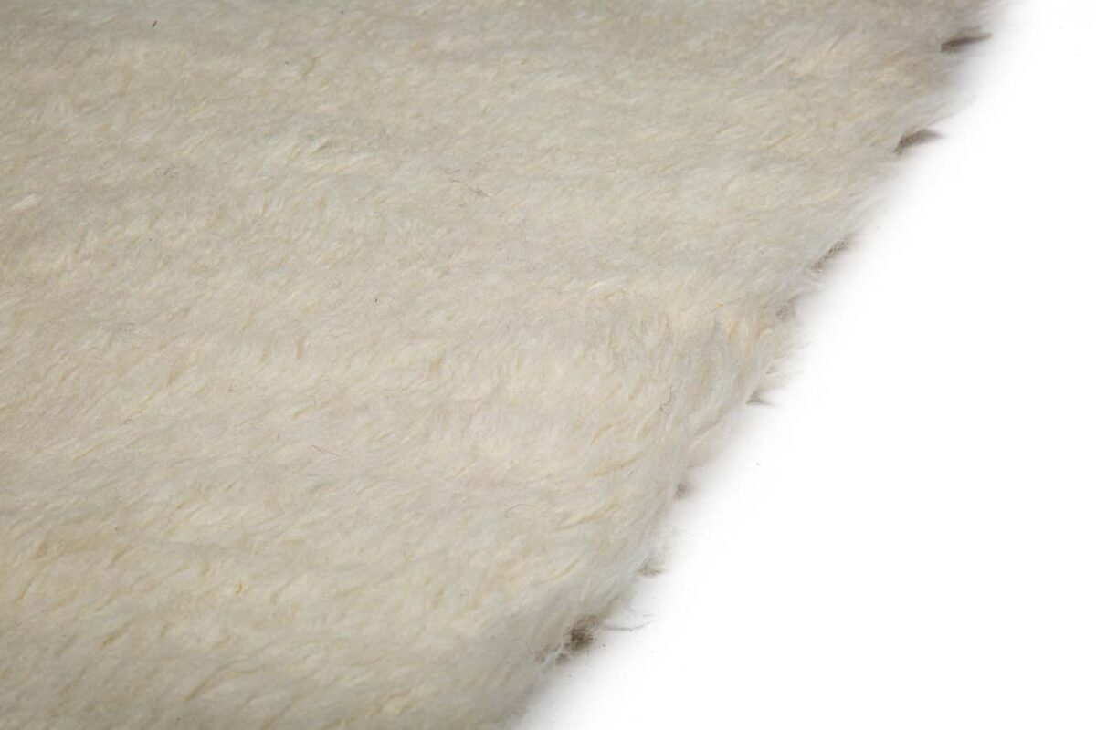 Close-up van Merano White 011 200x300, een zachte, gebroken witte donzige stof met een licht ongelijkmatige textuur. De foto benadrukt de pluizige vezels van het materiaal, wat warmte en comfort suggereert.