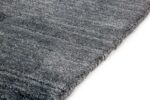 Close-up van de hoek van het Portofino Blue 01 200x300 vloerkleed op een witte achtergrond. Het zachte, geweven oppervlak met subtiele kleurvariaties en een dikke, afgewerkte rand zijn zichtbaar.