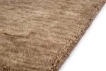 Close-up van de gestructureerde hoek van het San Stefano Camel 09 200x300 beige wollen tapijt, met de nadruk op de geweven vezels en het zachte oppervlak tegen een witte achtergrond.