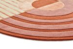 Een close-up van de Fano Girare Lychee ø280, een rond modern tapijt met geometrische patronen in terracotta, roze en crème met concentrische bogen, een centrale cirkel en parallelle crèmekleurige strepen.