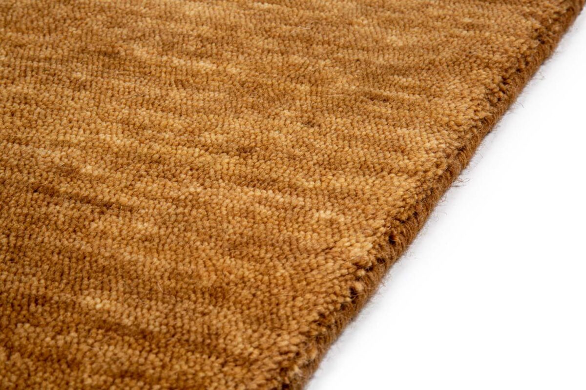 Close-up van het San Stefano Rust 10 200x300 tapijt, met een bruin geweven oppervlak met textuur, een subtiel patroon en zichtbare vezels. De rand van het tapijt is duidelijk te zien op de voorgrond op een witte achtergrond.