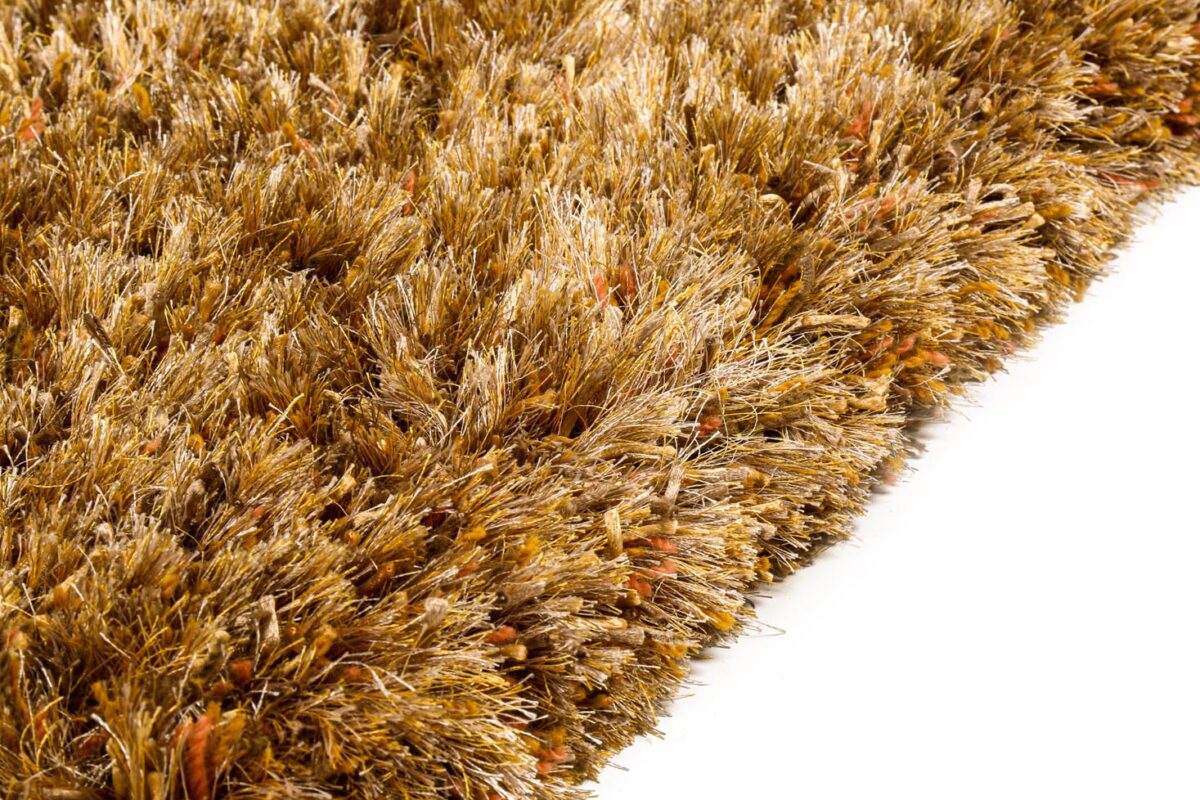 Close-up van het New Paulo Gold 030 200x300 vloerkleed, met dikke, getextureerde bruine en gouden vezels met oranje getinte draden. Het pluche shaggy tapijt rust op een wit oppervlak.