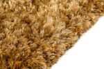 Close-up van het New Paulo Gold 030 200x300 vloerkleed, met dikke, getextureerde bruine en gouden vezels met oranje getinte draden. Het pluche shaggy tapijt rust op een wit oppervlak.