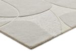Een close-up van het Bolsena Lago Grey 300x271 vloerkleed toont abstracte, gebogen vormen in lichtbeige en crèmekleurige tinten, met een modern ontwerp met zowel gladde als subtiel verhoogde structuurdelen.