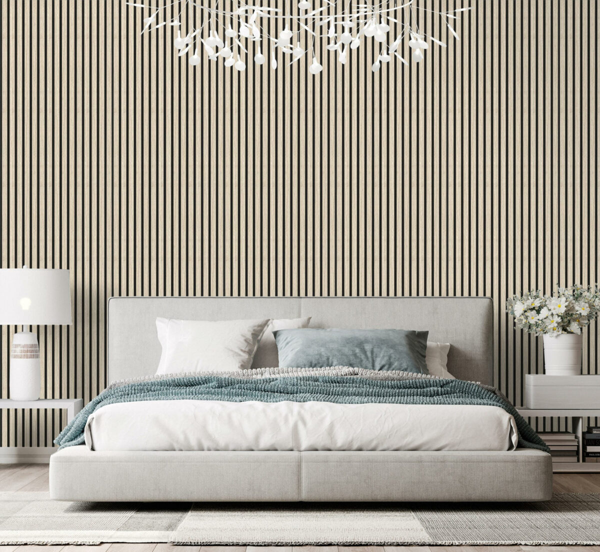 Een moderne slaapkamer met een laag grijs bed, blauw en wit beddengoed, twee witte nachtkastjes met lampen, een vaas met bloemen en een accentmuur met akoestische panelen Akupanel Eiken Light Naturel 270x60 cm. Boven het bed hangt een kroonluchter met witte bladeren.